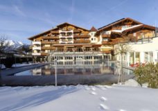 Frontansicht Alpenpark Hotel im Winter mit Schnee auf der Wiese vorm Außenpool