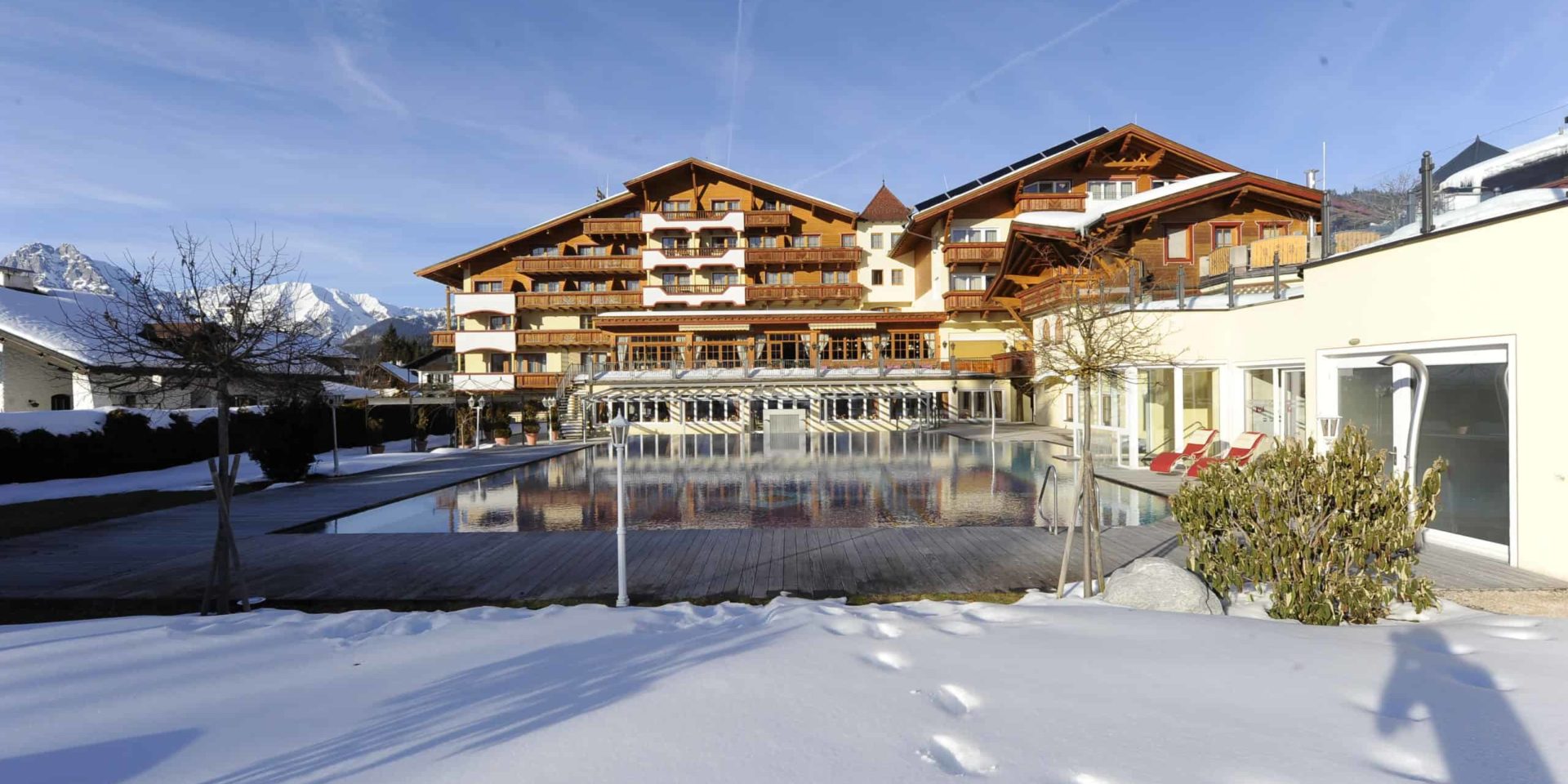 Frontansicht Alpenpark Hotel im Winter mit Schnee auf der Wiese vorm Außenpool