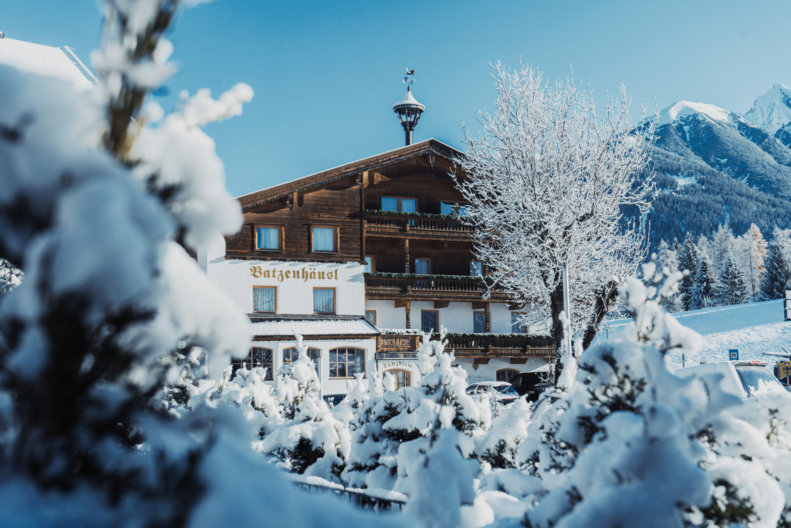 Frontansicht Gasthof Batzenhäusl im Winter umgeben von Neuschnee und blauem Himmel